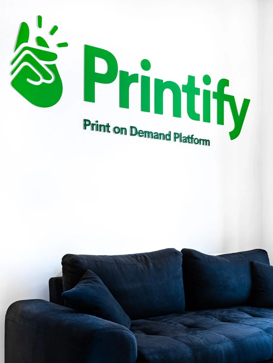 Zaļš Printify logotips uz sienas virs dīvāna